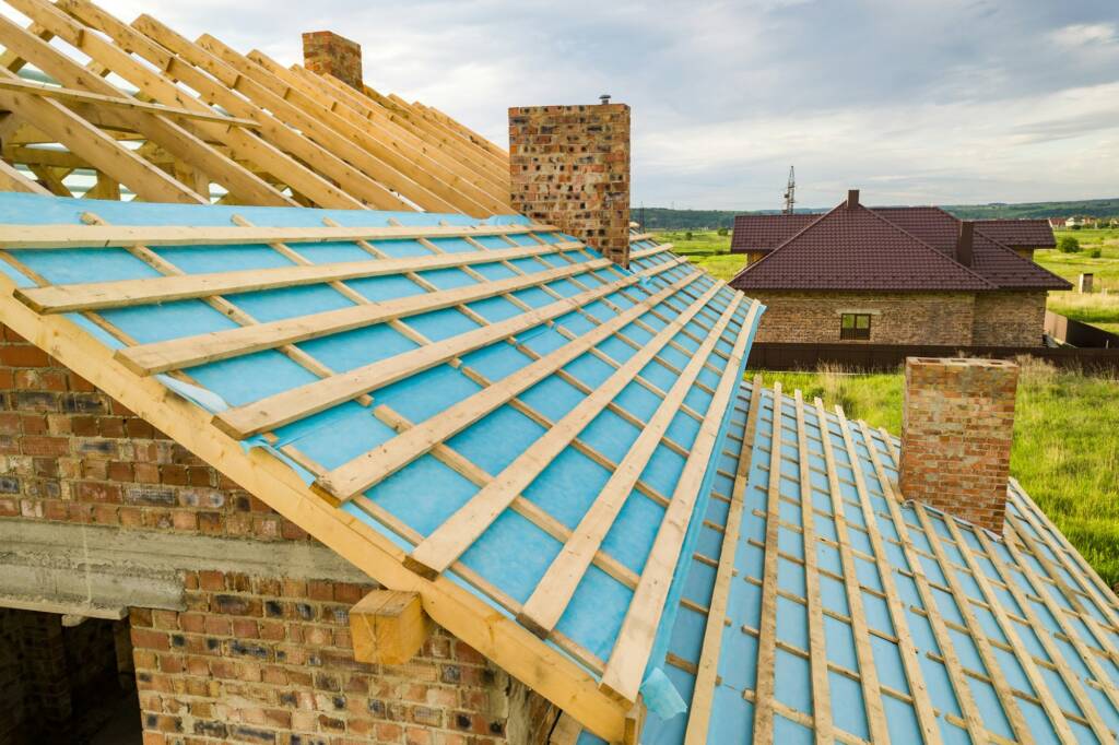 Aerial view of a brick house with wooden roof frame under construction.