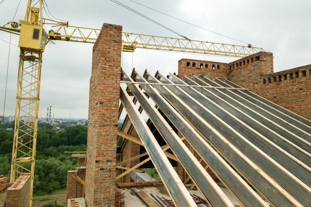Unfinished brick apartment building with wooden roof structure under construction.